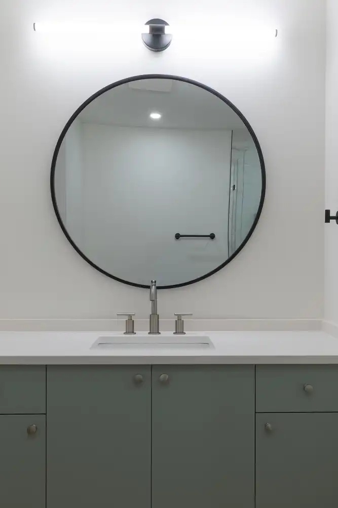 Renovated bathroom vanity with a round mirror and green cabinetry